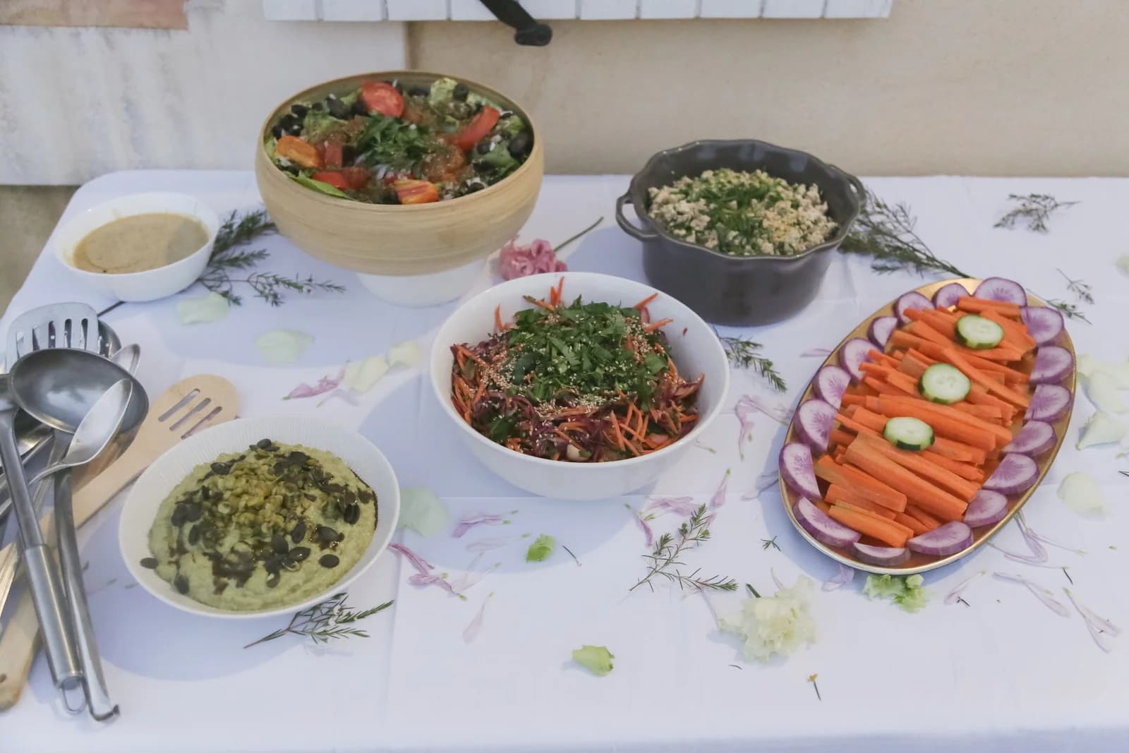 Buffet fleuri sur nappe blanche : salades, houmous, crudités, pétales et romarin. Photo : Joséphine