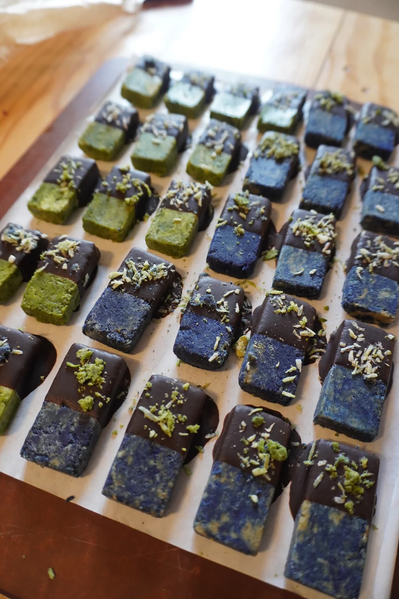 Des bouchées vertes et bleues, trempées dans le chocolat cru et poudrées de noix de coco, alignées sur un plateau