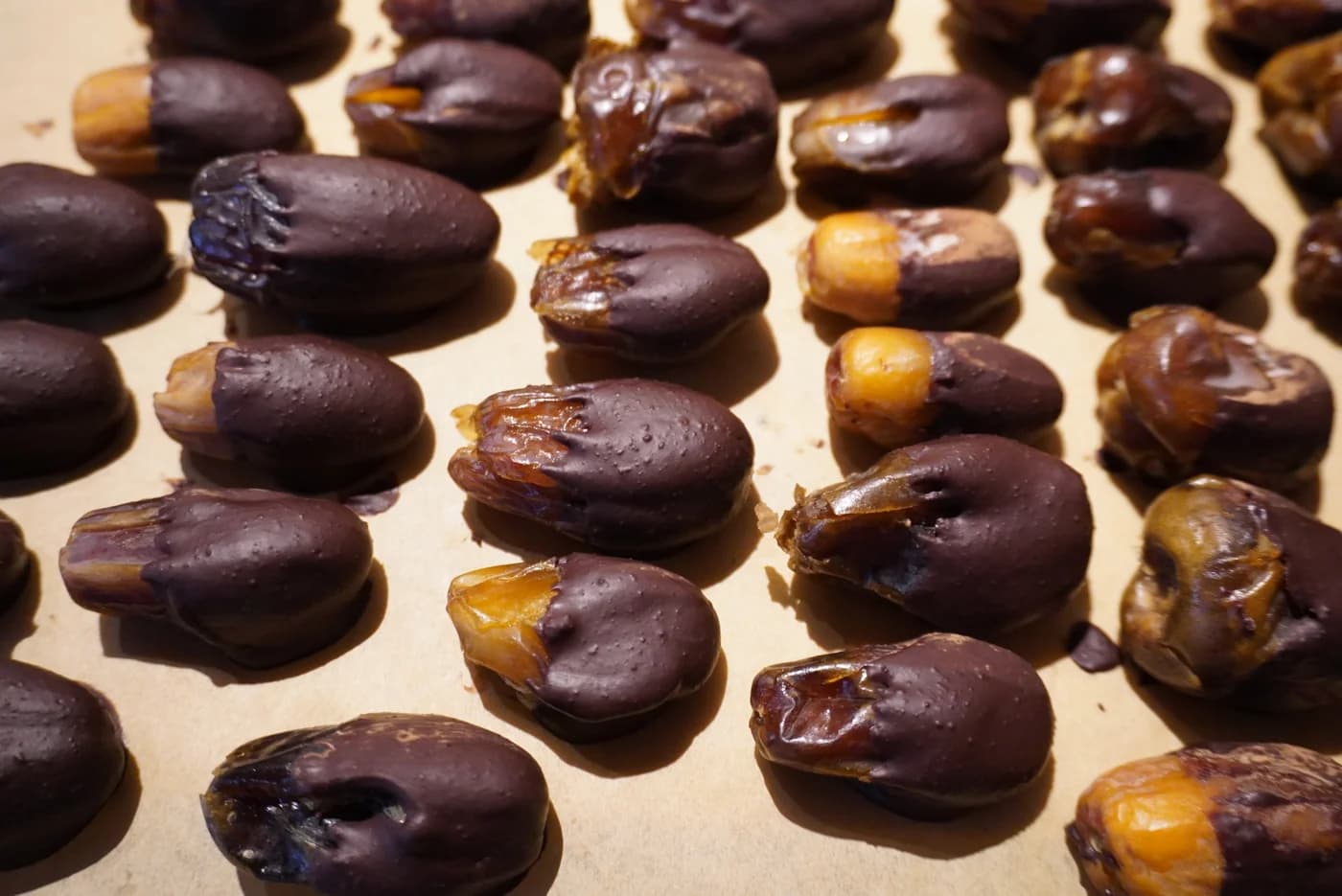 Des dattes trempées dans le chocolat cru, alignées sur le papier, la chair dorée qui dépasse