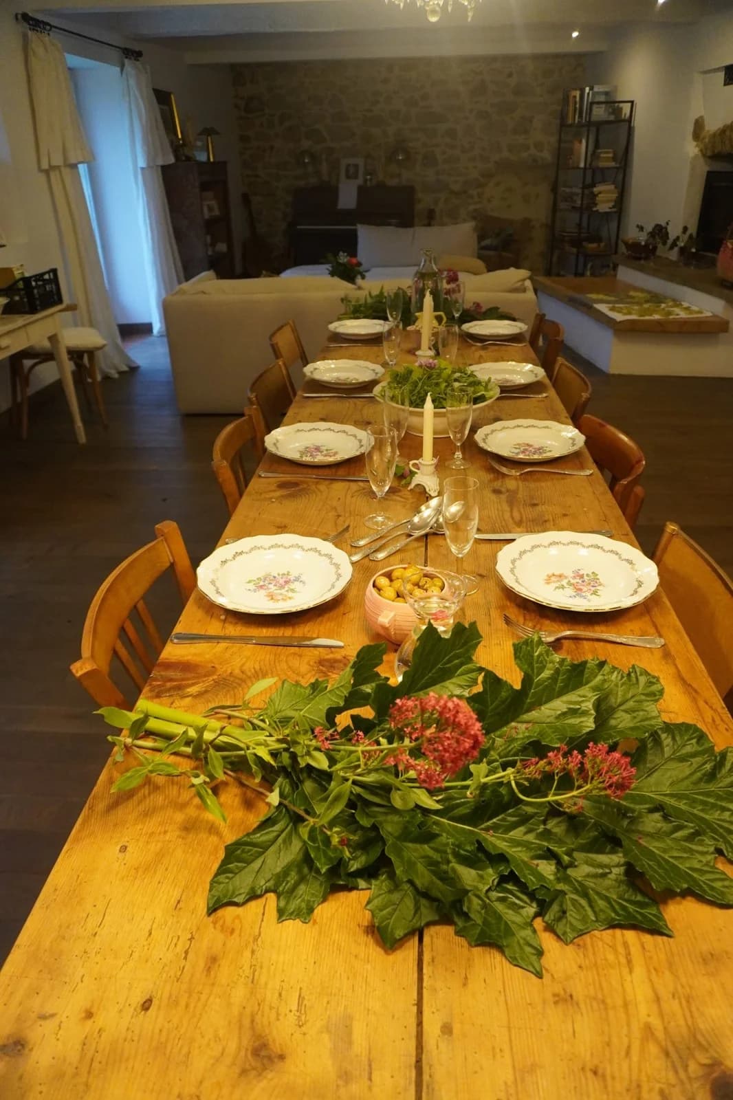 Une longue table en bois dressée, bougies et feuillage au centre