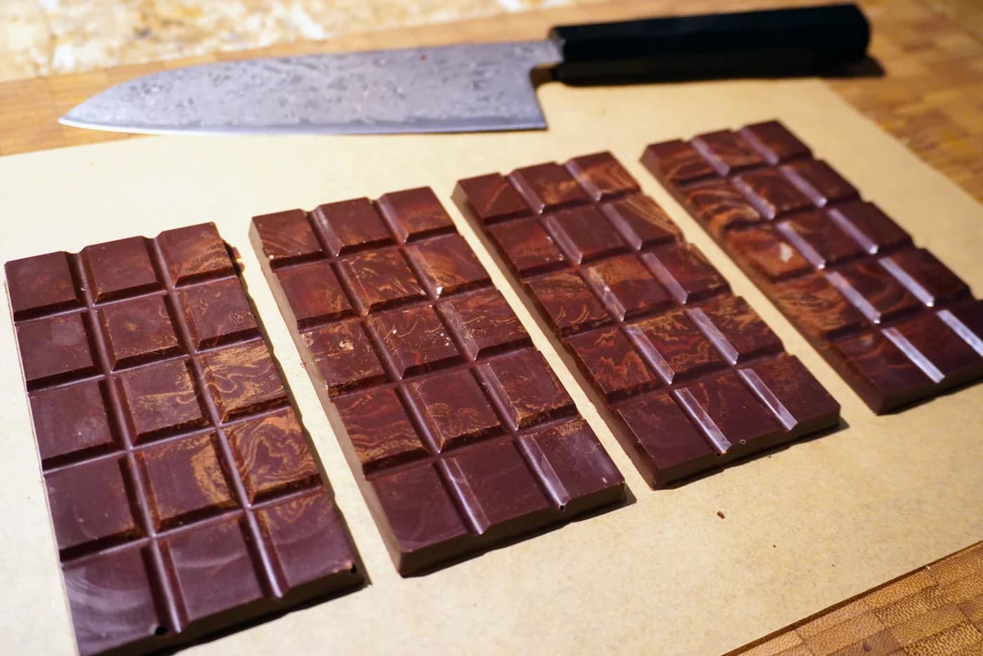 Quatre tablettes de chocolat cru marbrées, posées sur le papier, un couteau japonais derrière
